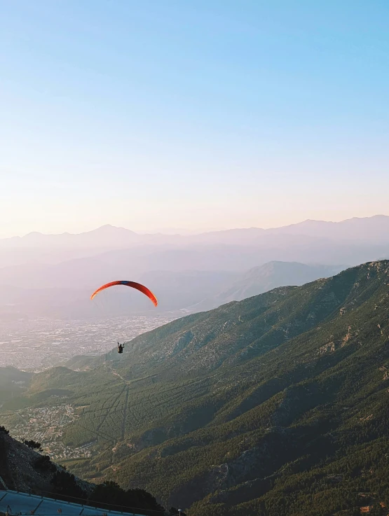 a paraglider soaring above a vast green hillside