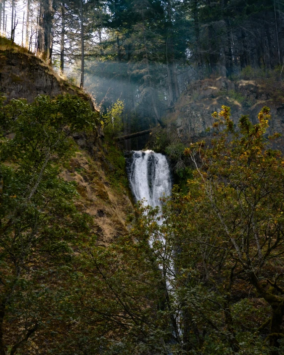 a waterfall with fog over it and surrounded by trees