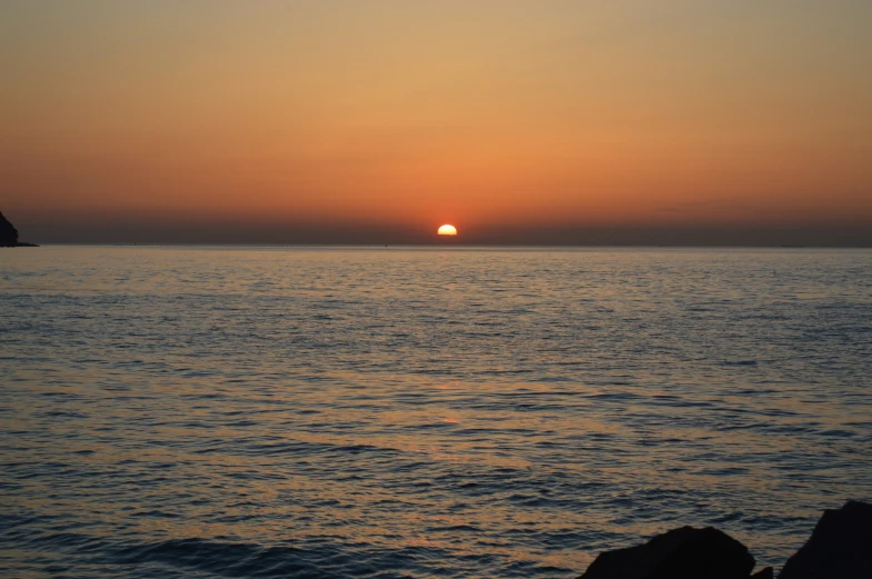 a sunset seen over the water in front of a rocky cliff