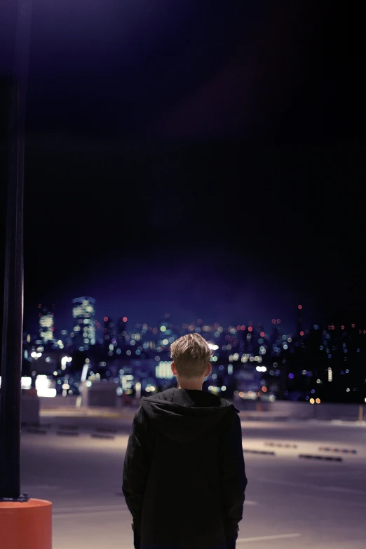 a man standing on the sidewalk with city lights behind him