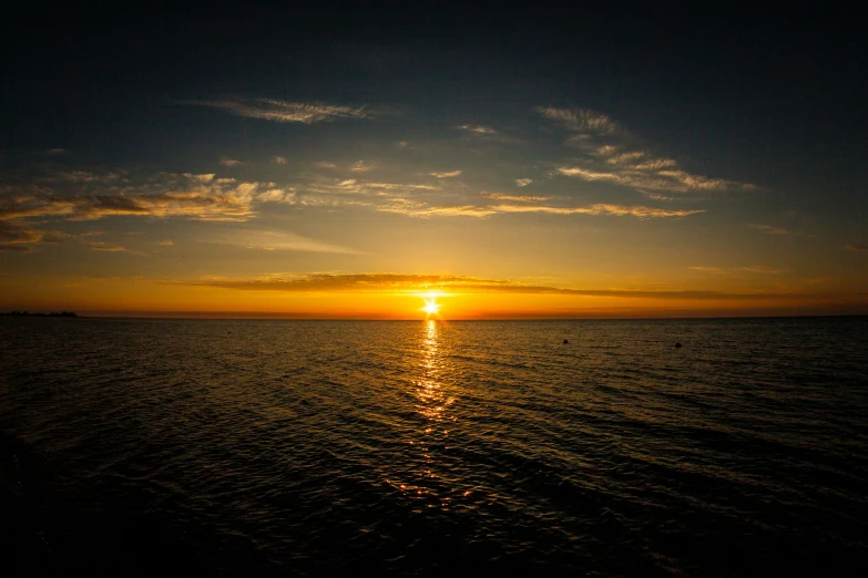 a sun setting behind the ocean with small clouds