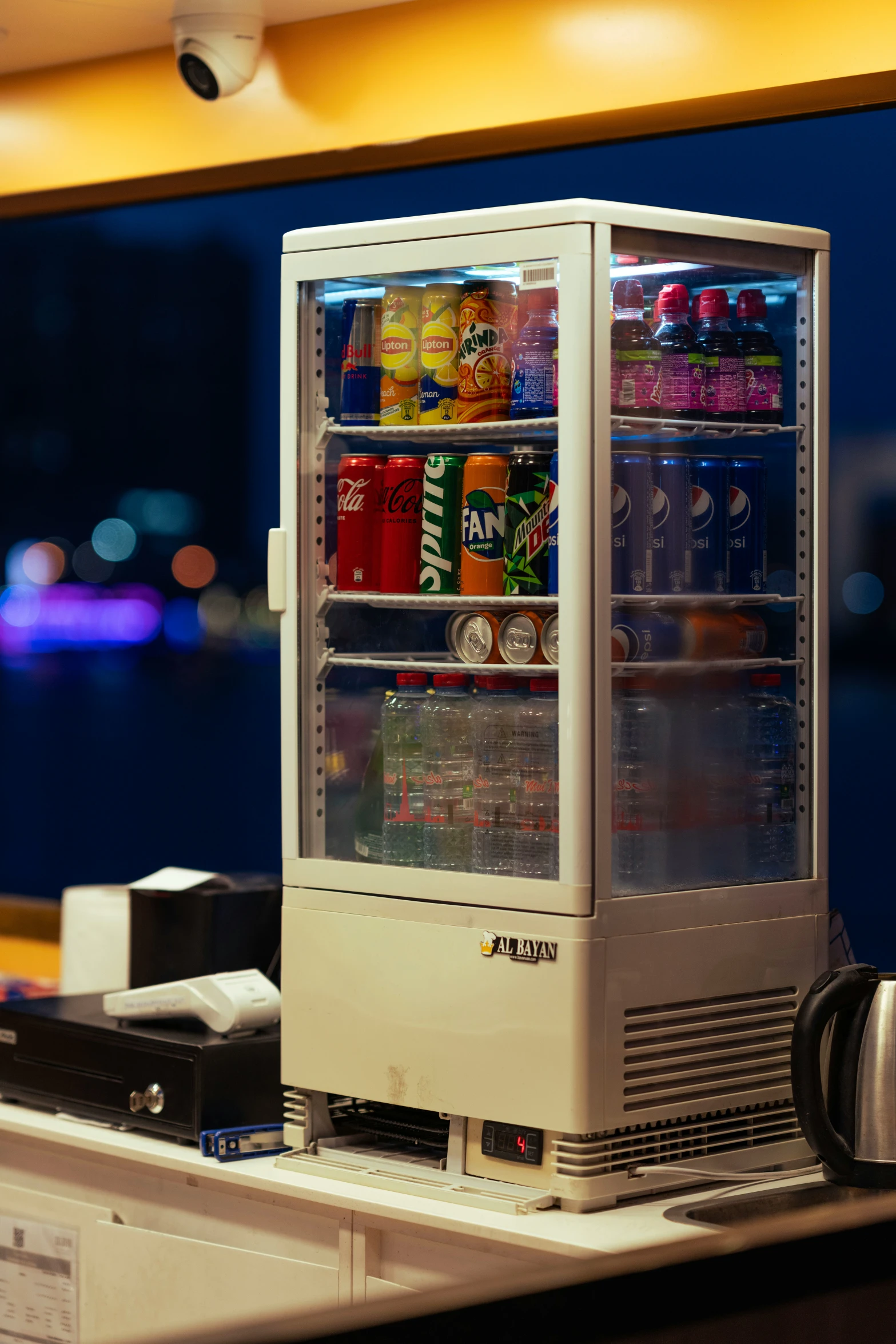 a refrigerated refrigerator in the foreground with a bottle of soda and drinks inside