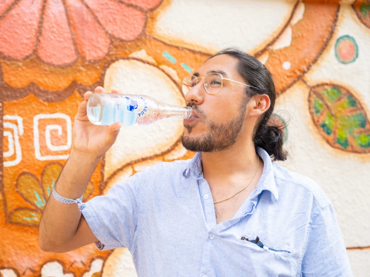 a man drinking water with a large mural behind him