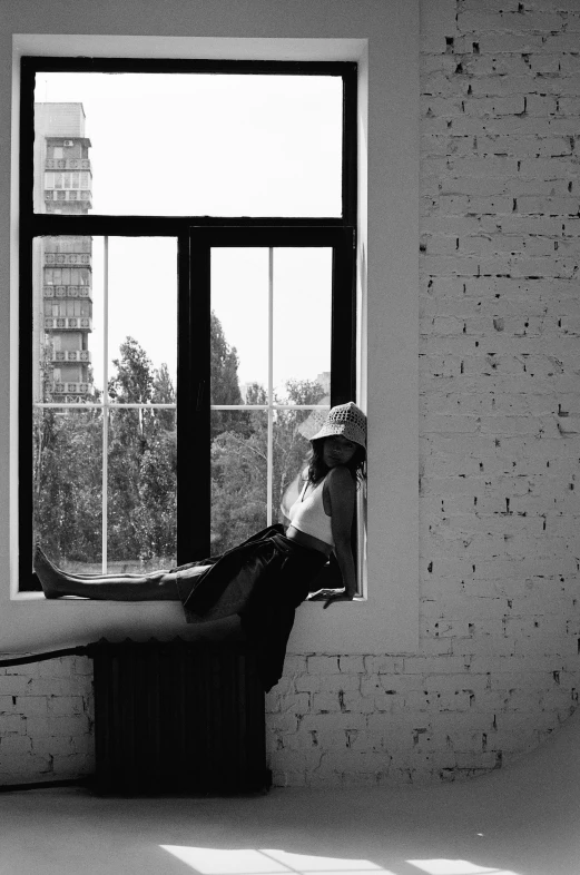 the woman sits on a window sill while looking out the window