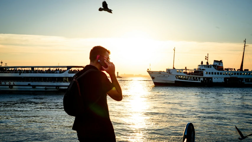 a man standing on the shore while talking on his cell phone