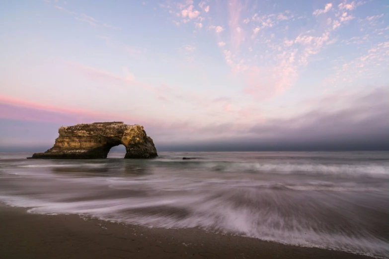 an ocean scene with a large rock on the side of it