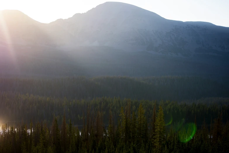 a mountainside with trees in the foreground and the sun shining through the mountains