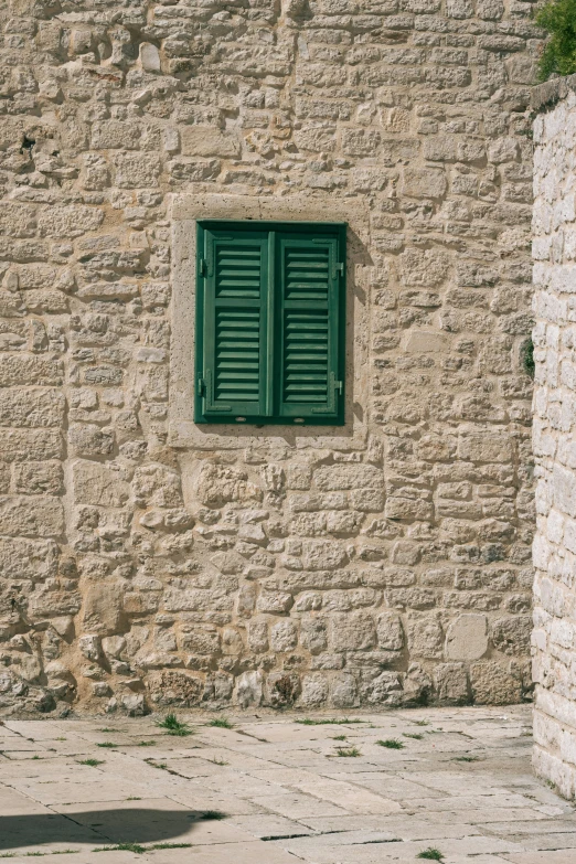 an old brick wall and window with green shutters