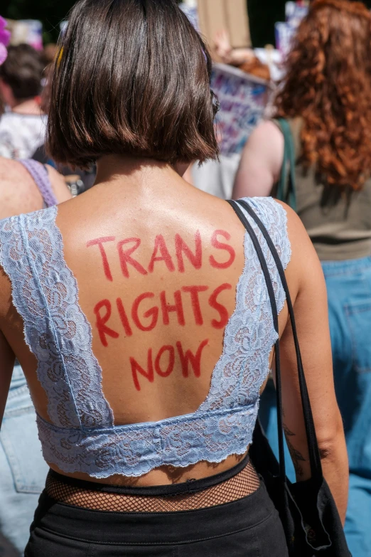 a woman wearing a trans rights shirt with the words trans's rights now painted on her back