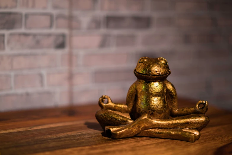 golden statue frog sitting on wood with brick wall in background