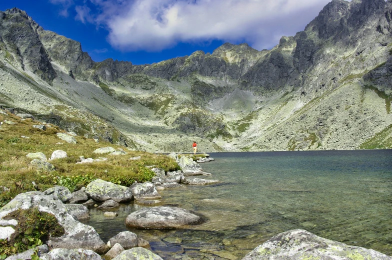 a man stands near the edge of a stream in a mountainous area