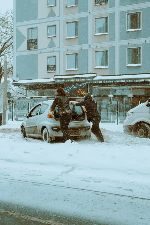 two people hing the car on the snow covered street