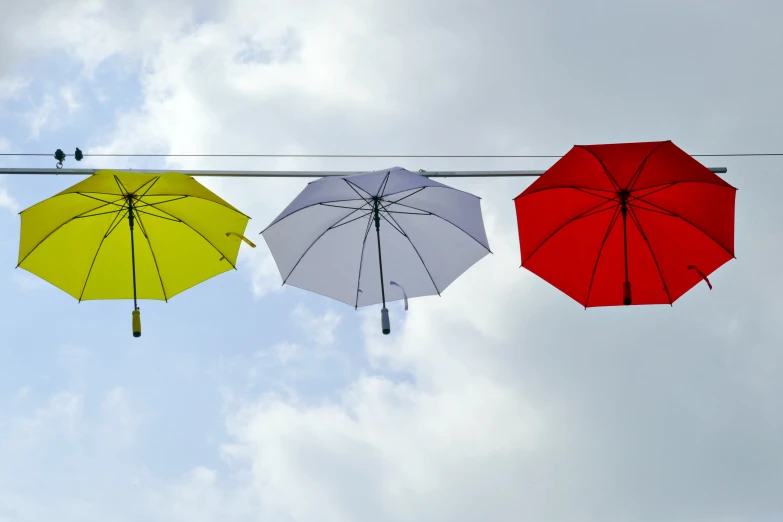 three open umbrellas on power lines against a cloudy sky