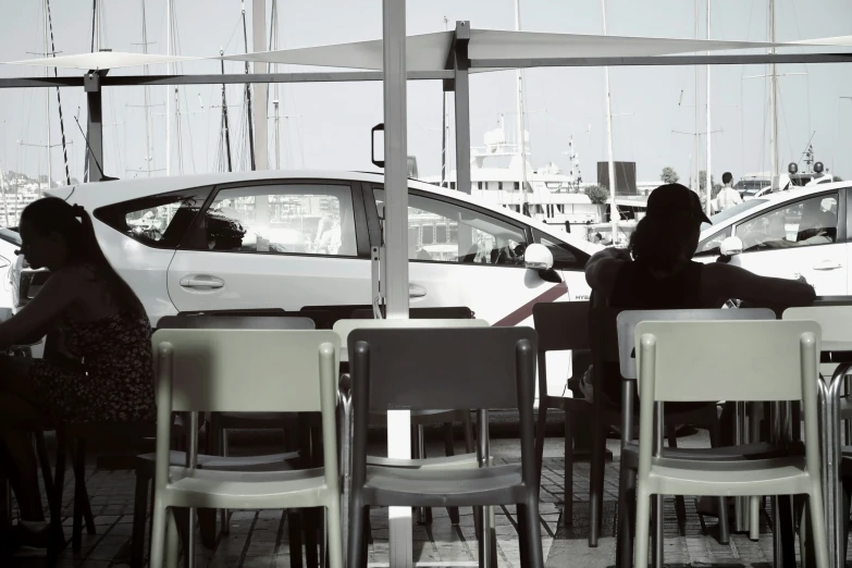 a person sitting at an outdoor cafe with parked cars behind them
