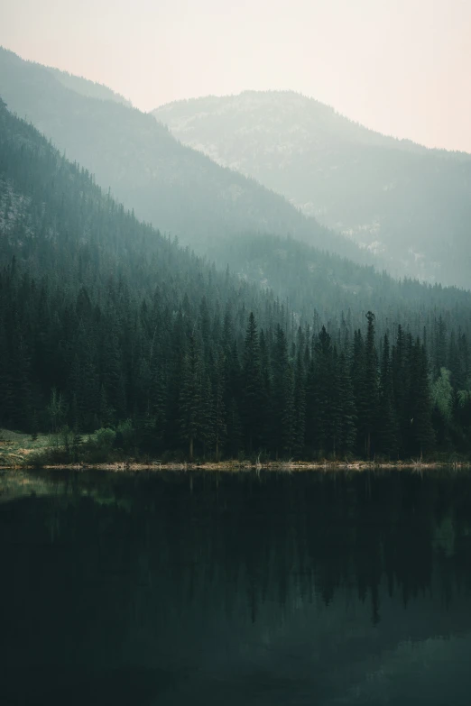 the trees in the mountains are reflecting on the water