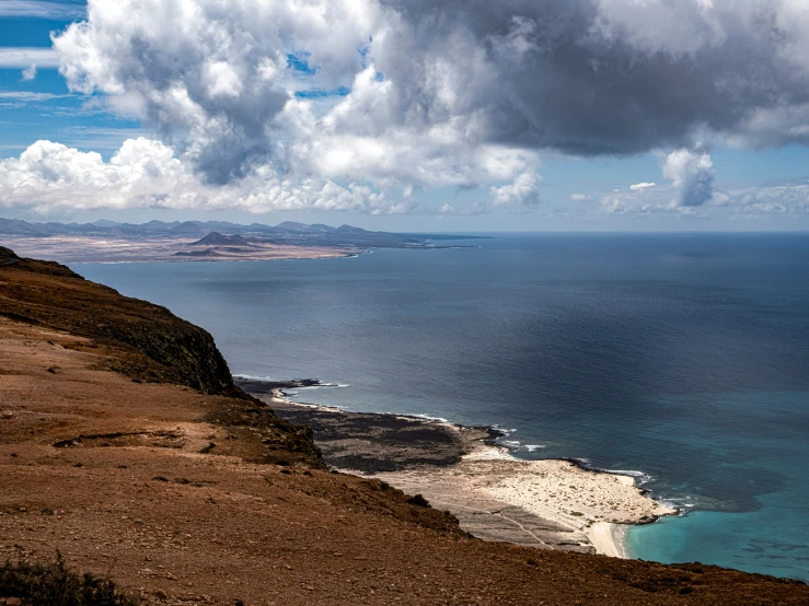 an ocean view of a mountain side with some clouds in the sky