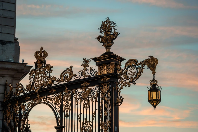 the golden wrought iron gate is flanked by an antique street light