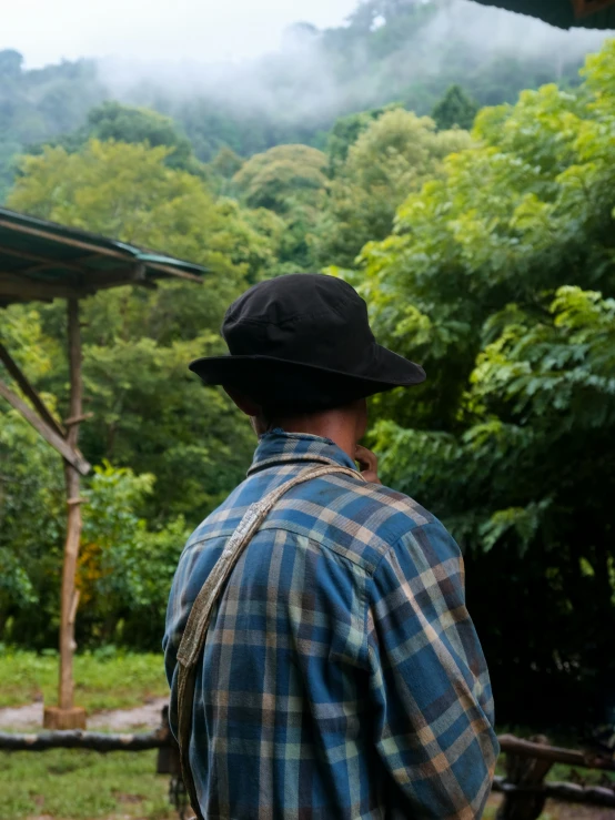 a man in a hat standing on a lush green hillside