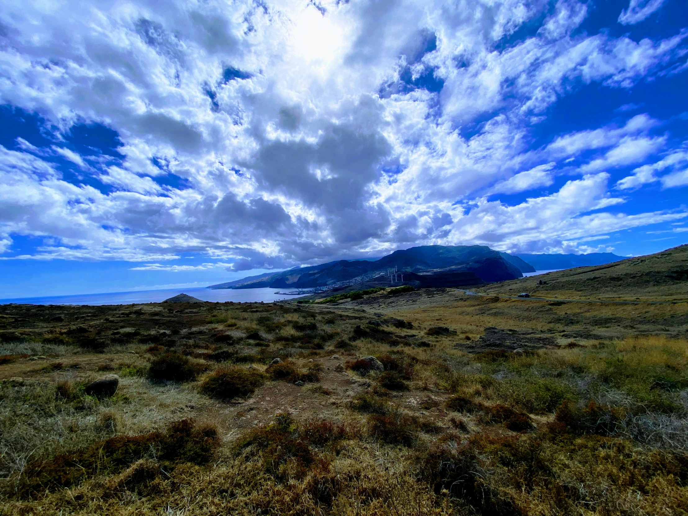 a view of some hills, trees and water under a cloudy blue sky