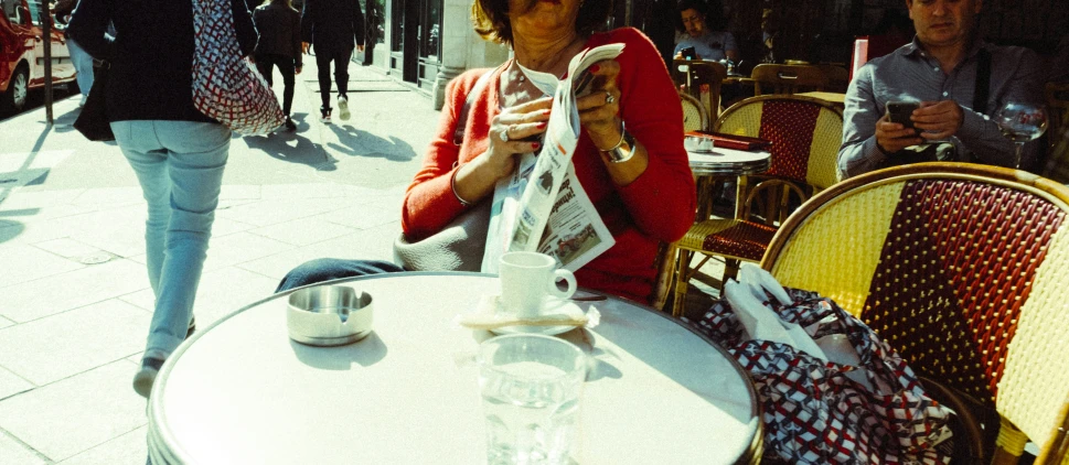 a woman sits at an outdoor table with a cup and coffee