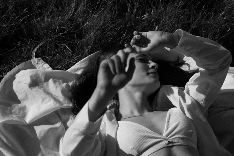 a woman lays in the grass, while talking on her cell phone