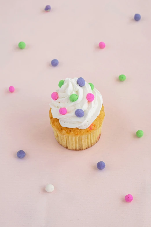 a cupcake on a pink surface, surrounded by colorful candies