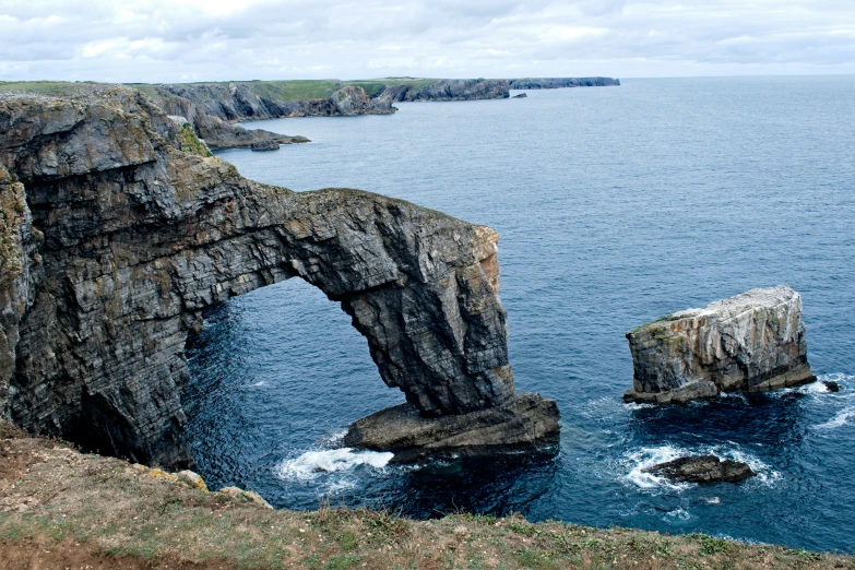 the ocean with an arch in it is seen on a cloudy day