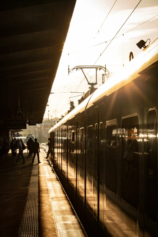 people are walking at a station next to a train