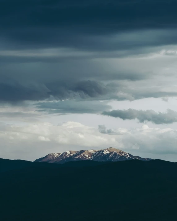 a dark sky and a distant snow capped mountain with white clouds