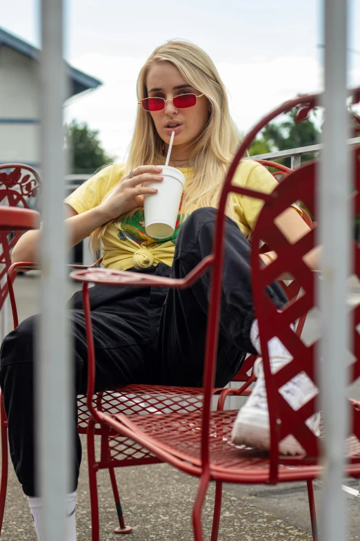 a blond woman wearing sunglasses sitting at a red metal table