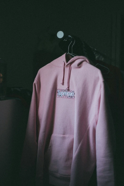 a pink hoodie hanging from a hanger with a logo