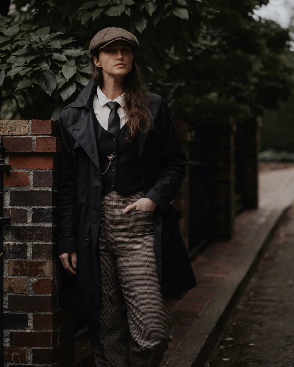 young woman in black jacket and plaid skirt standing near brick wall