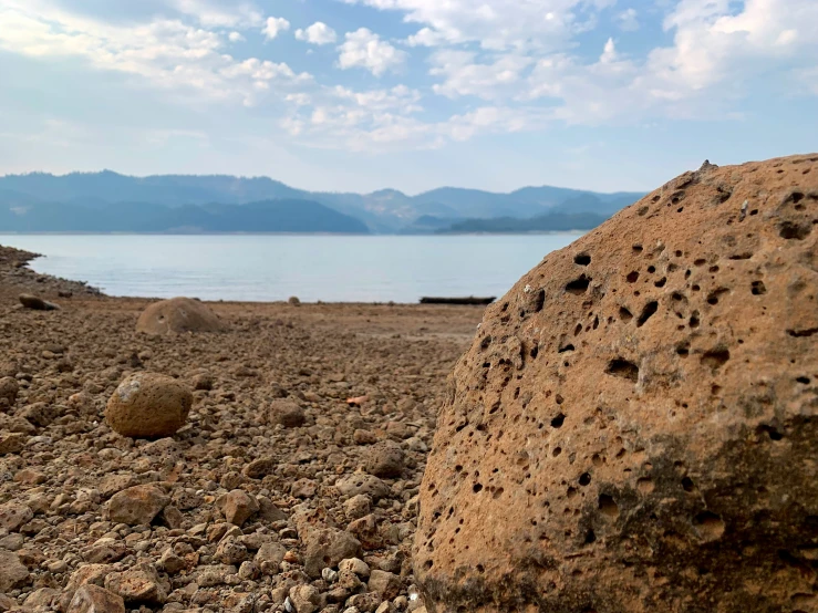 a large rock on the shore of a lake with holes in it