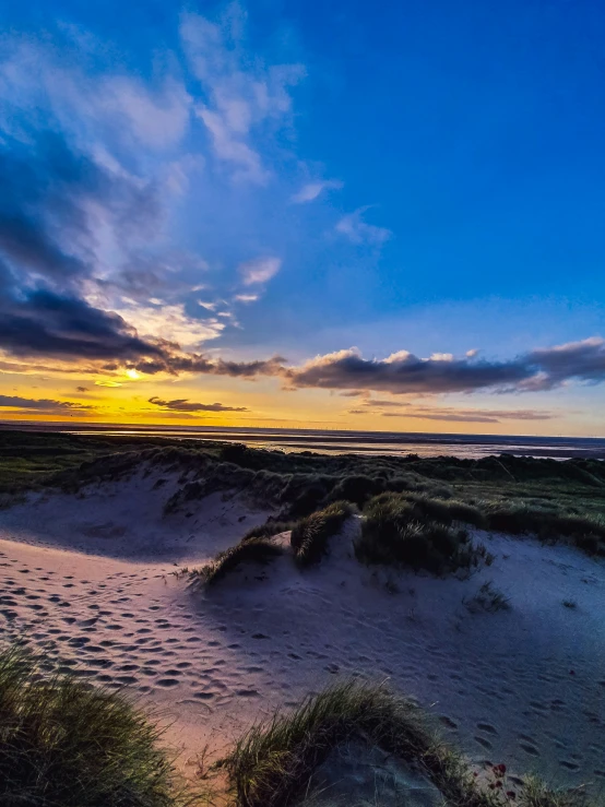 sun setting on a sandy beach near grass