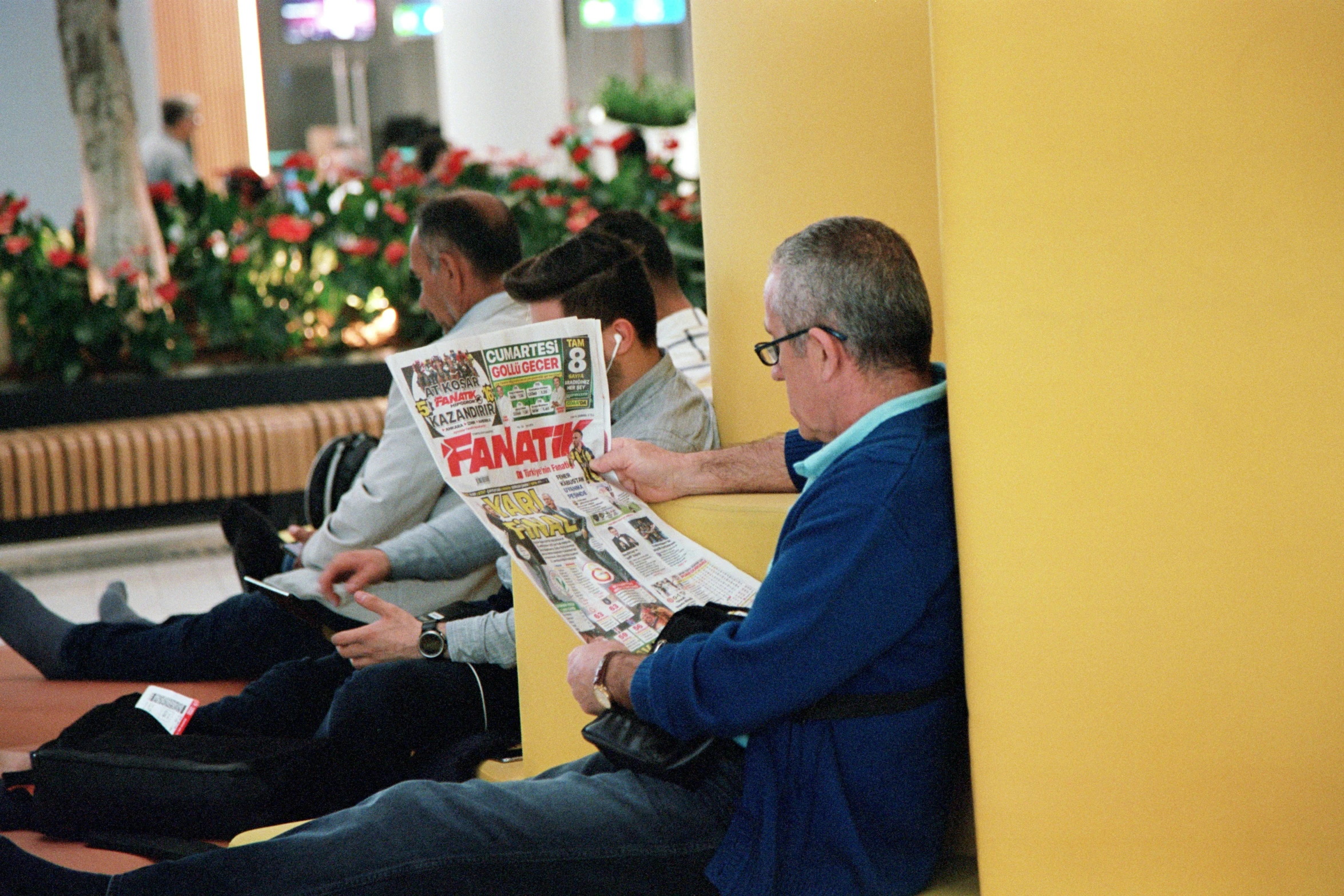 three people sitting on benches with their legs crossed and one man looking at a newspaper