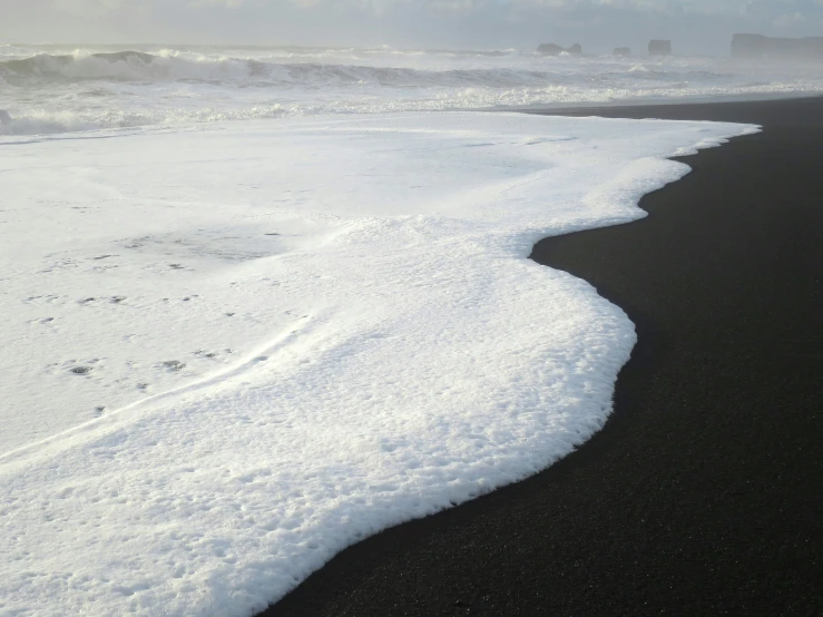 a sandy beach with snow on the bottom and white waves in the water