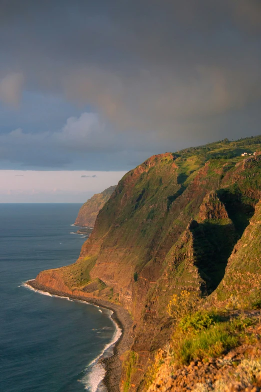 large cliff side next to the ocean under a cloudy sky