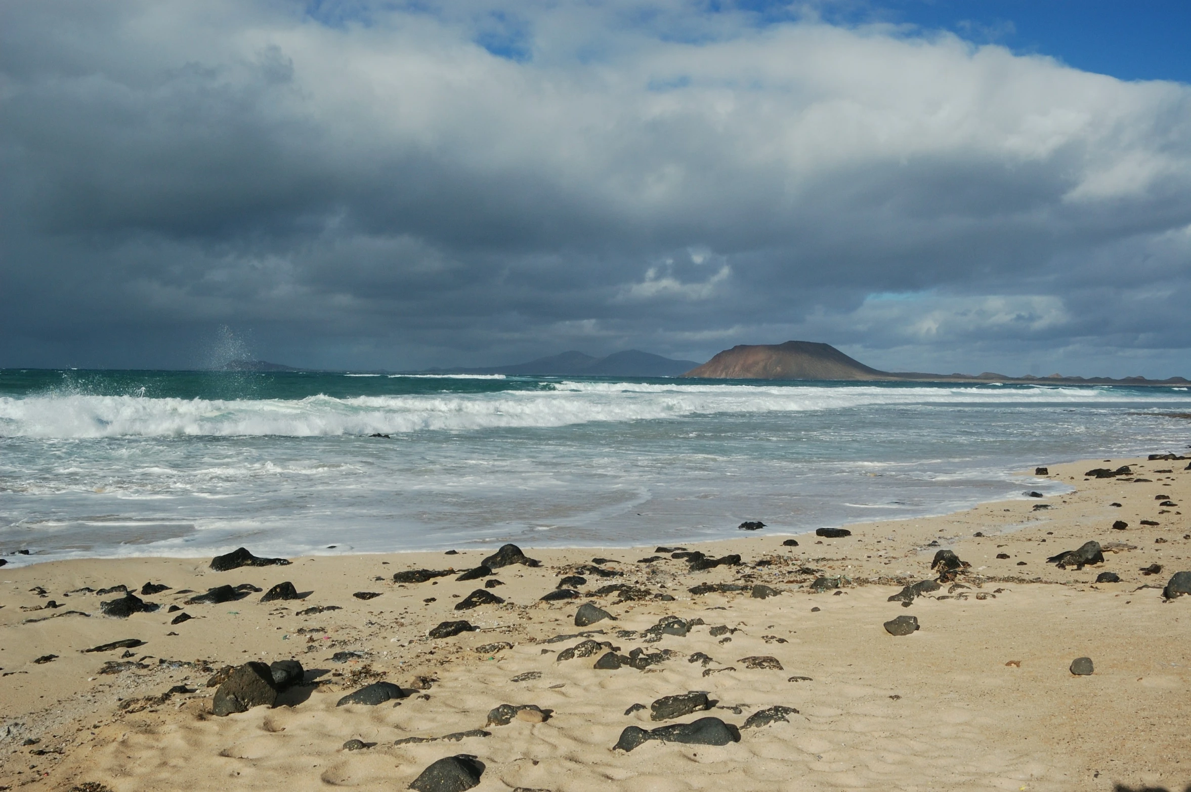 people walking along the beach near a mountain