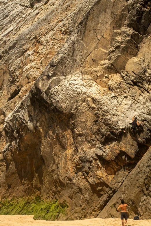 a man standing next to an ocean beach next to a big cliff