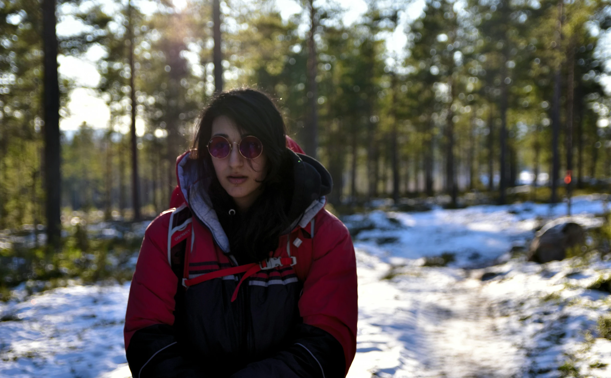 a young woman in sunglasses standing next to trees in the snow