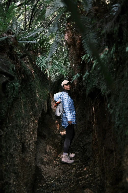 a man in blue jacket standing in dirt tunnel with trees