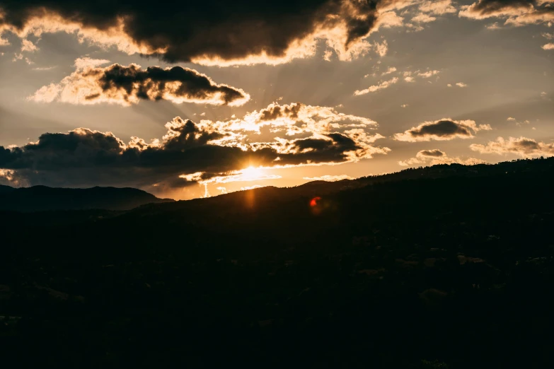 the sun is setting in the clouds over a mountain