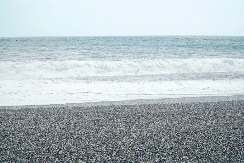 a lone person holding a surfboard stands in the water at the beach