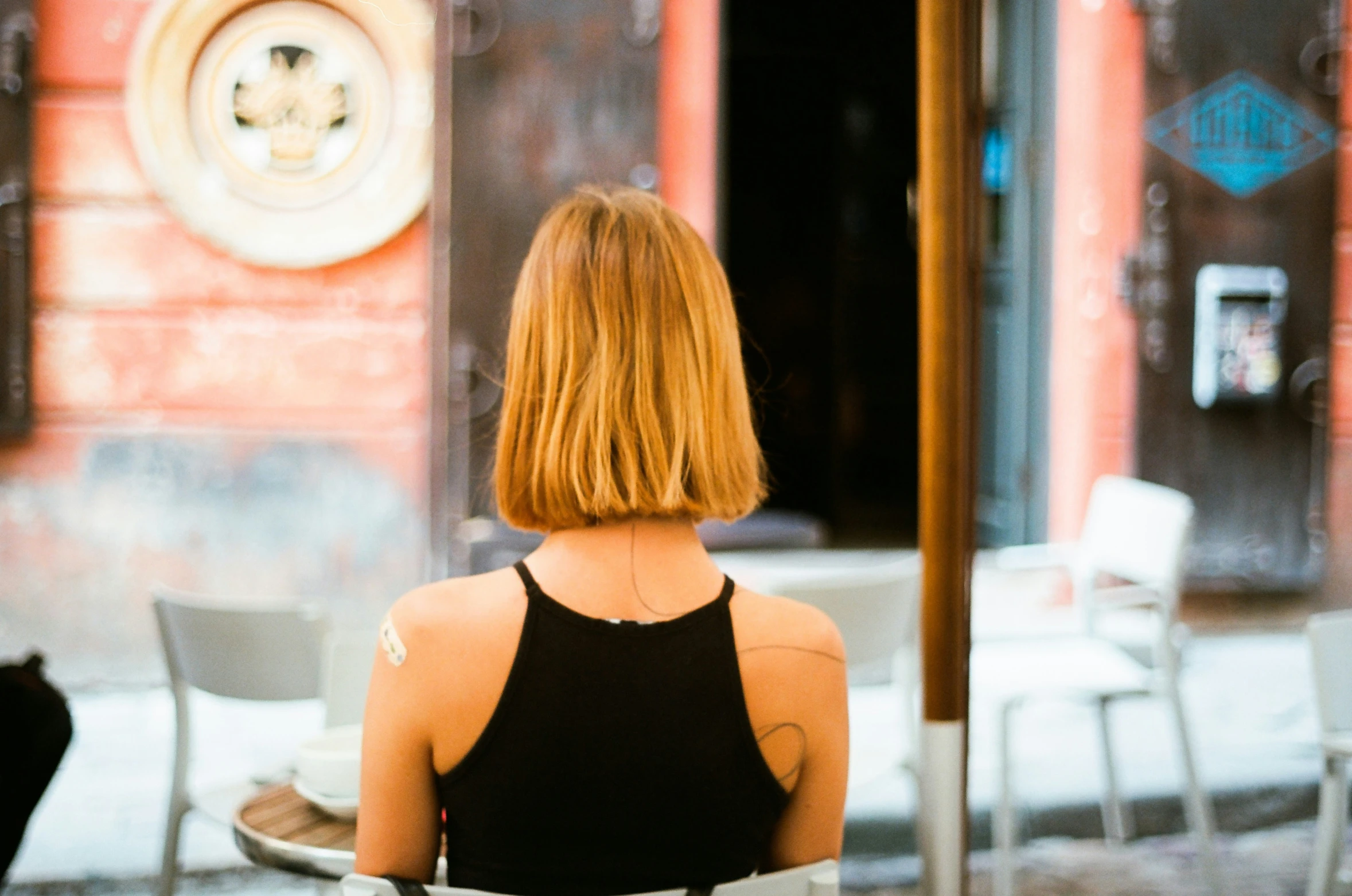 the back of a woman's head standing next to a table and chairs outside