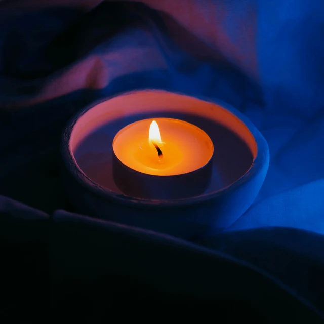 a lit candle sitting on a purple fabric