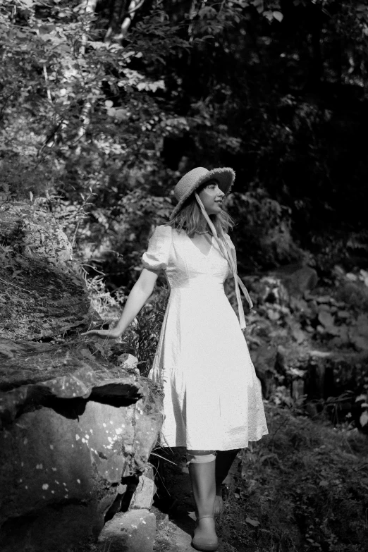 a woman in a hat stands on a rock near some trees