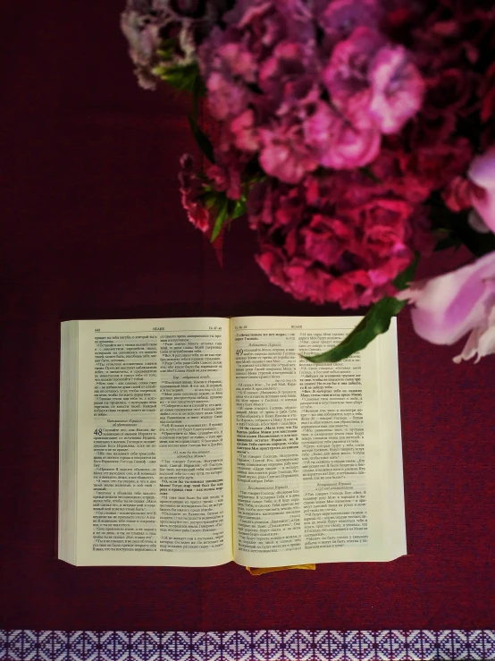 open book on table next to flowers on purple table cloth