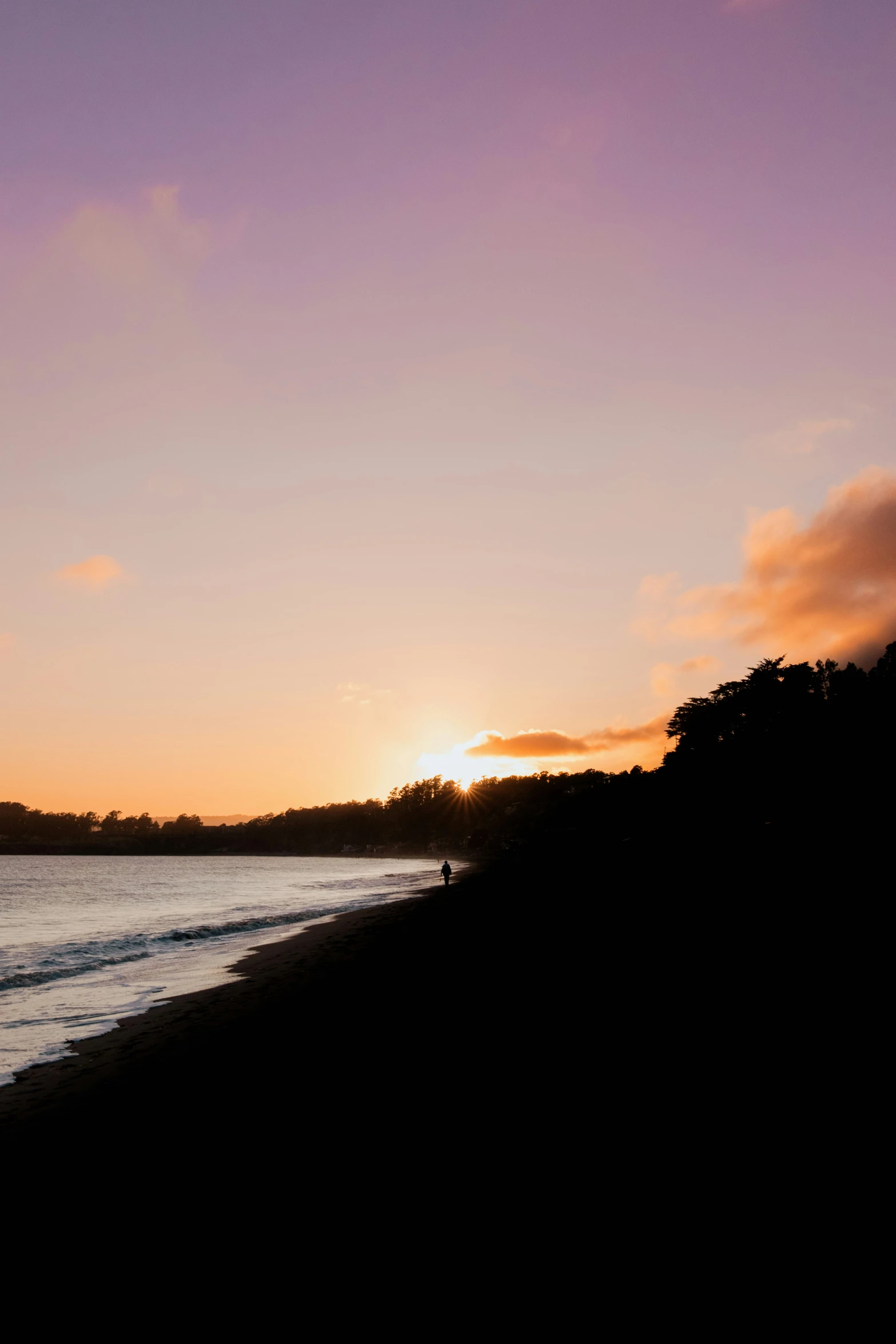 the sun is setting behind a hill with a body of water in front of it