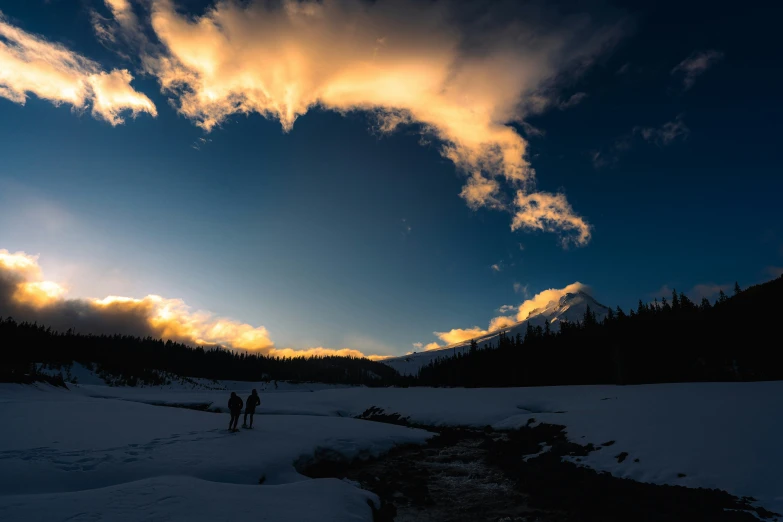 two people on skis stand beneath a beautiful sky