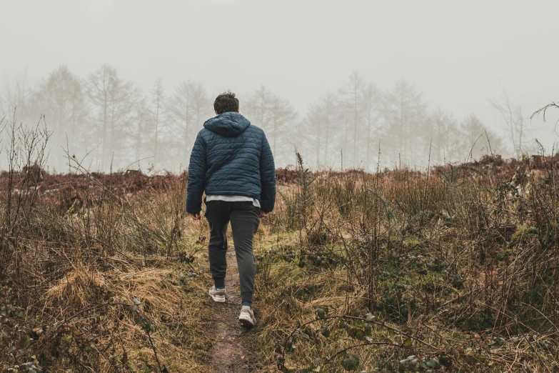 a man walking away from the camera through a field